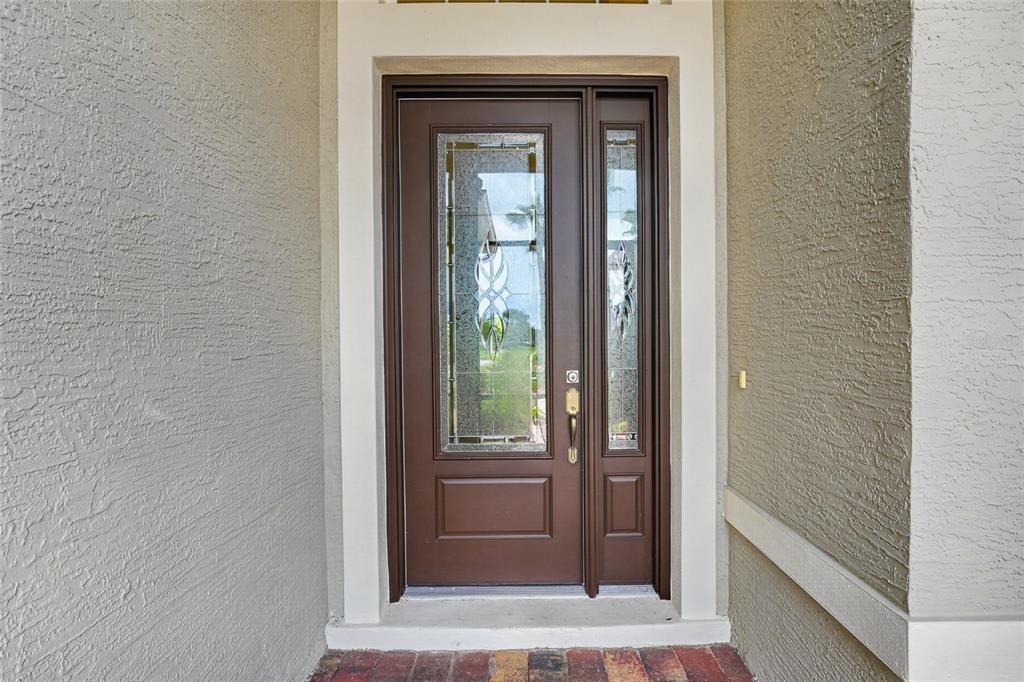 A brown front door with a glass insert and sidelight sits in a stucco entryway — 10216 JULIA ISLES AVENUE, OXFORD, FL