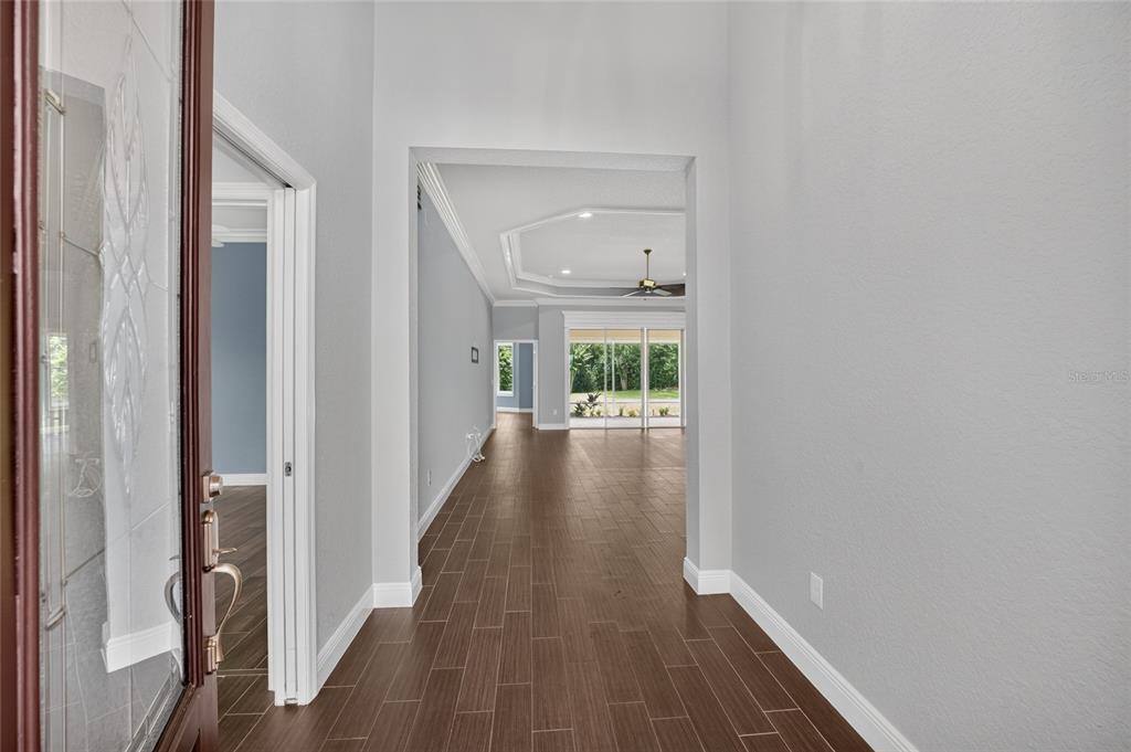 A bright entryway features wood-look tile flooring leading into an open living area with sliding doors — 10216 JULIA ISLES AVENUE, OXFORD, FL