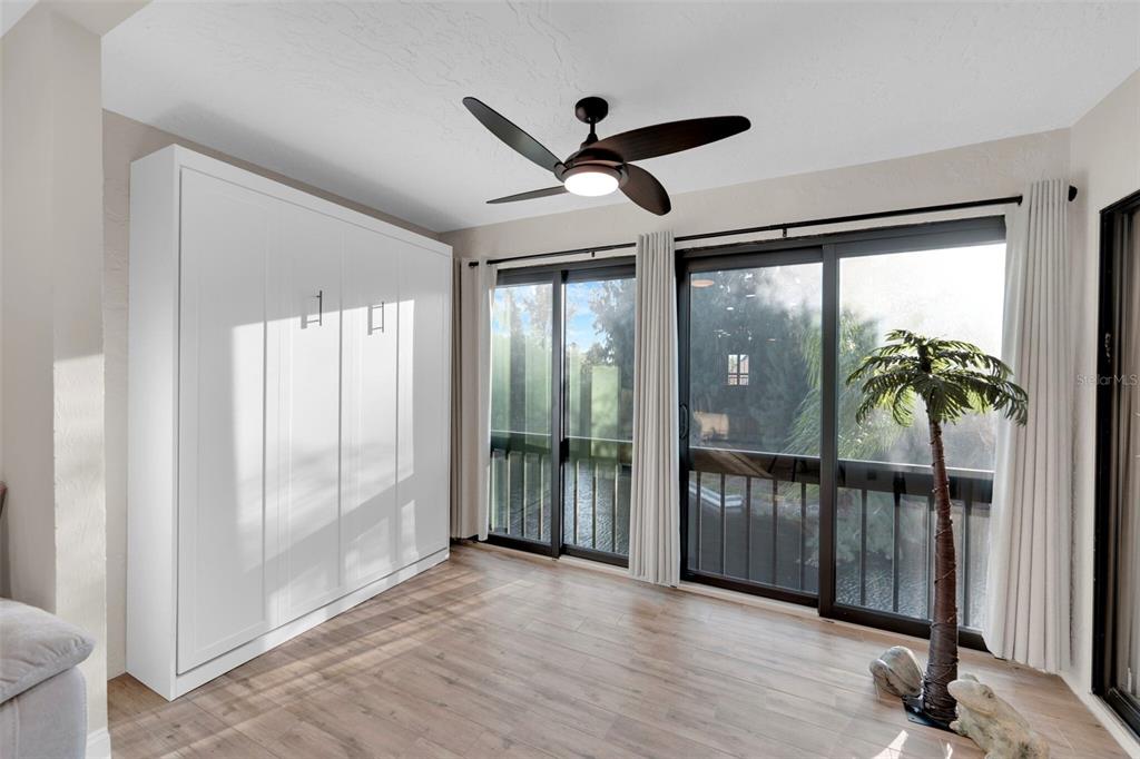 A room features a white Murphy bed, wood-look flooring, a ceiling fan, and sliding glass doors — 15761 WINDWARD WAY CIRCLE UNIT 3302, FORT MYERS, FL