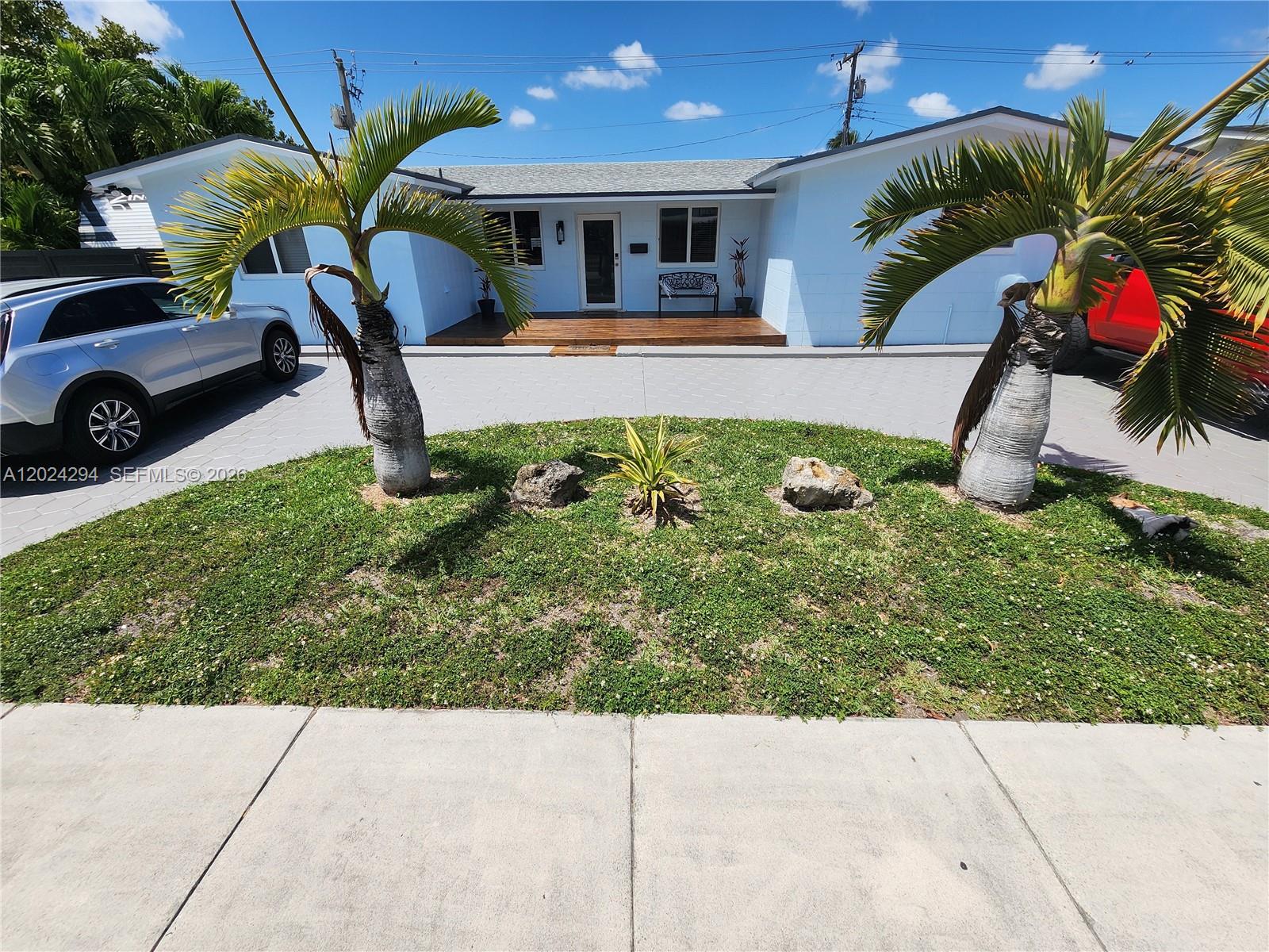 A light blue house features a wooden front deck, palm trees, and a paved driveway — 9591 SW 52nd Ter, Miami FL 33165, MIAMI, FL