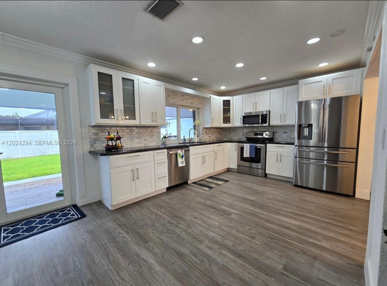 A modern kitchen features white cabinets, stainless steel appliances, dark countertops, and light wood flooring — 9591 SW 52nd Ter, Miami FL 33165, MIAMI, FL