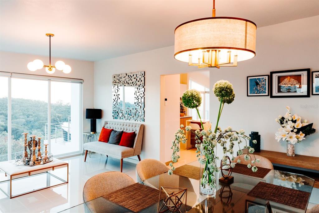 A dining room with a glass table, modern chandelier, and a view of green hills — KM 0.7 PR-551, JUANA DIAZ, PR