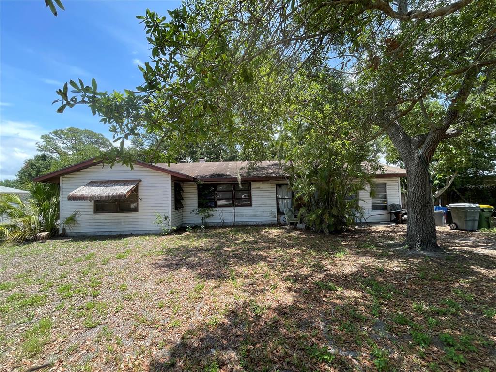 A single-story house with white siding and a brown roof sits behind a large tree — 1311 S BRINK AVENUE, SARASOTA, FL