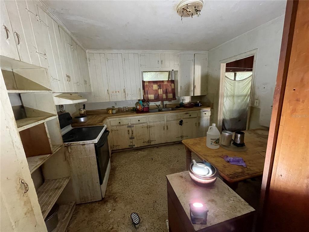 A dated kitchen features white wooden cabinets, a stove, a wooden table, and worn flooring — 1311 S BRINK AVENUE, SARASOTA, FL