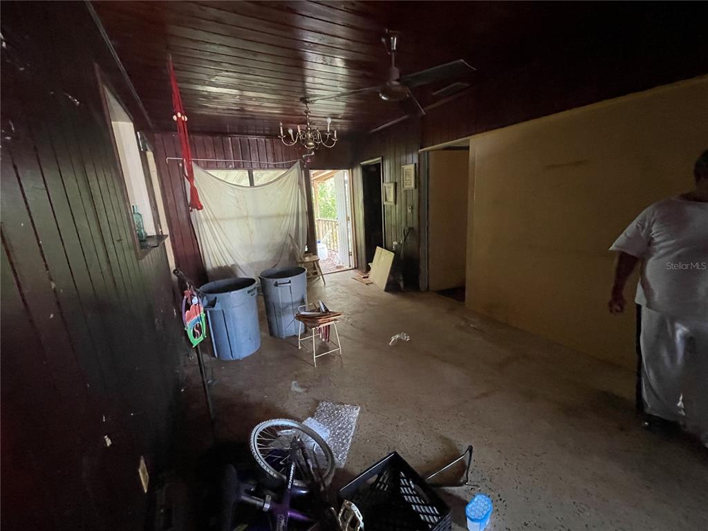A cluttered room with dark wood-paneled walls, a ceiling fan, and a concrete floor — 1311 S BRINK AVENUE, SARASOTA, FL