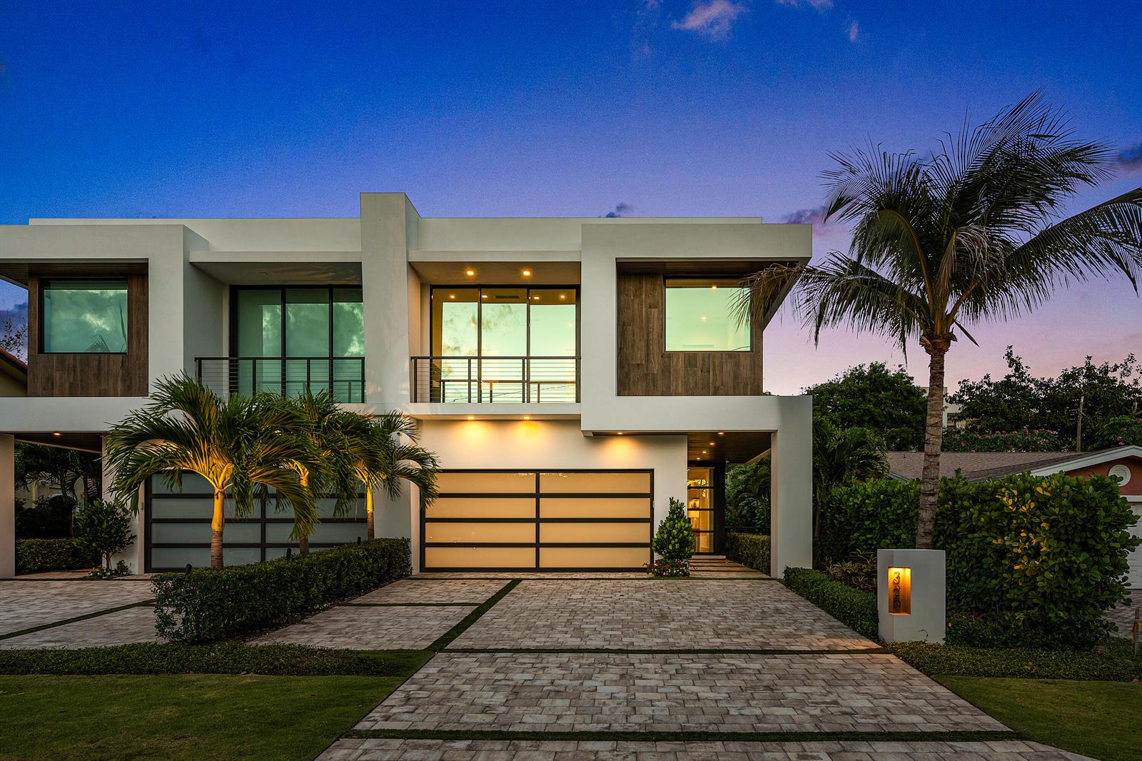 A modern two-story house with a paved driveway, garage doors, and palm trees at dusk — 320 NE Wavecrest Way, Boca Raton FL 33432, BOCA RATON, FL