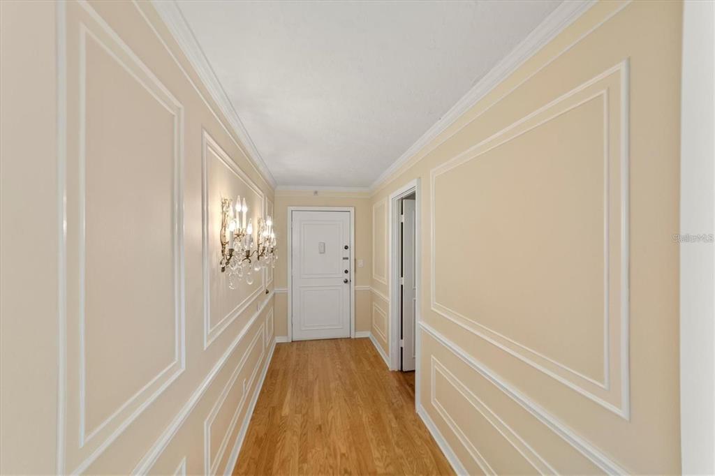 A hallway features light-colored walls with decorative molding, hardwood floors, and a crystal wall sconce — 1111 N GULFSTREAM AVENUE UNIT 16C, SARASOTA, FL
