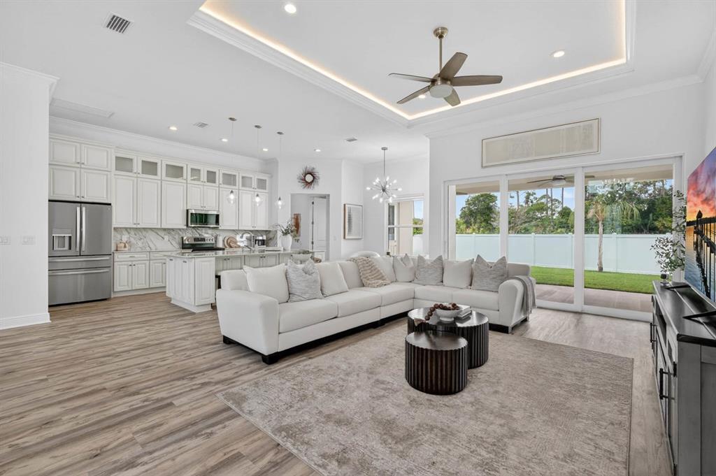 A bright open-concept living room and kitchen with white cabinetry, wood flooring, and sliding doors — 19 WESTCHESTER LANE, PALM COAST, FL