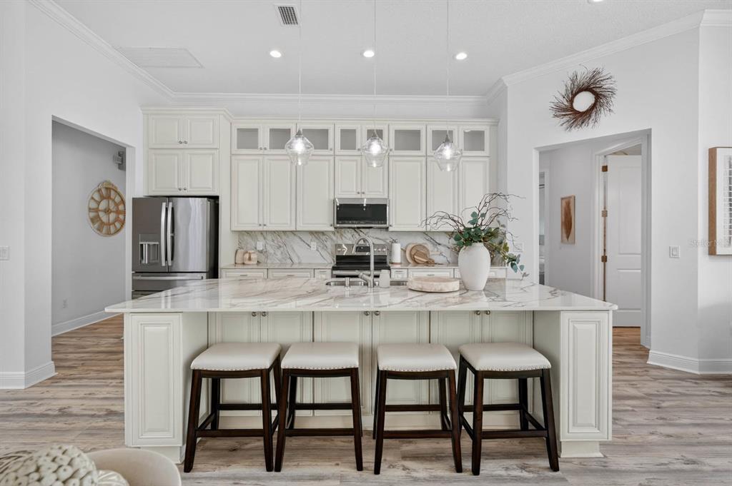 A kitchen features white cabinetry, a marble-topped island with four stools, and stainless steel appliances — 19 WESTCHESTER LANE, PALM COAST, FL