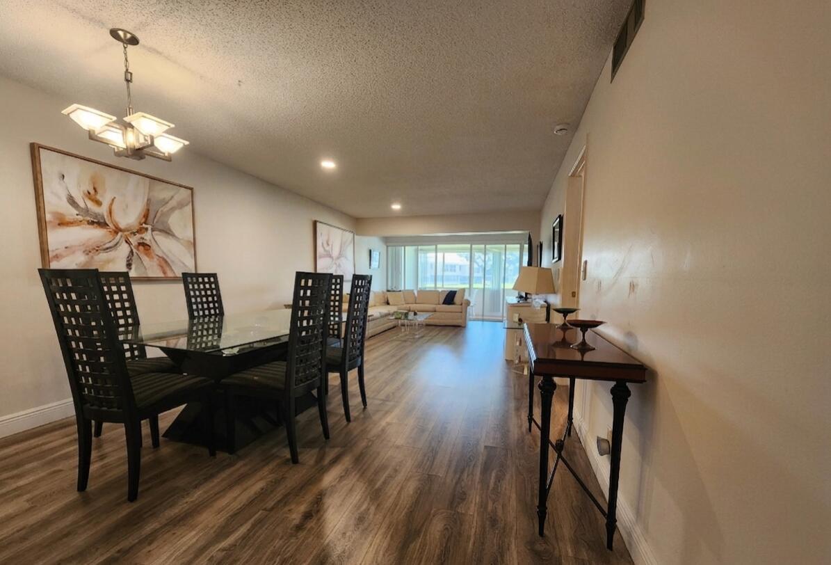 A dining area with a glass table and black chairs opens into a living room — 1560 NW 18th Avenue # 104, Delray Beach FL 33445, DELRAY BEACH, FL