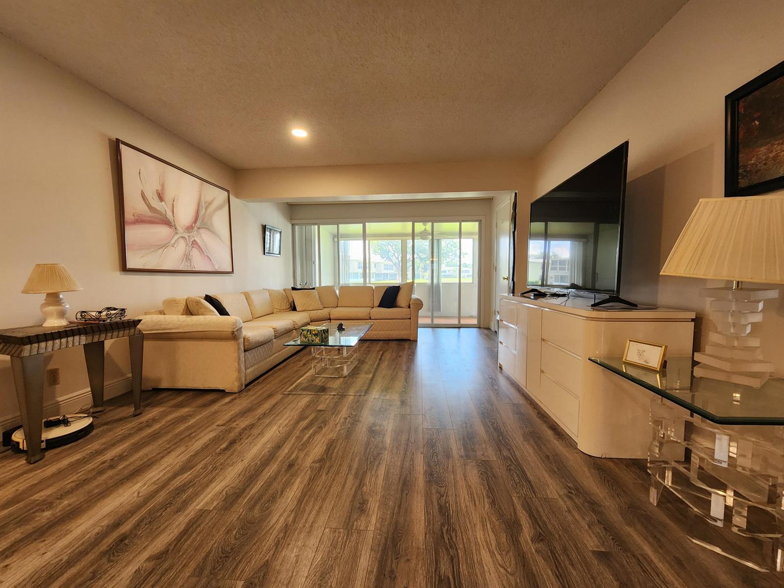 A living room with wood-look flooring, a large sectional sofa, and a television on a console — 1560 NW 18th Avenue # 104, Delray Beach FL 33445, DELRAY BEACH, FL