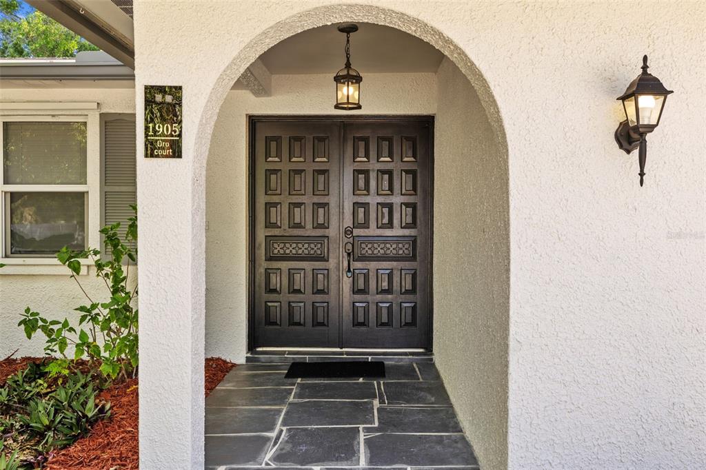 A dark double door with a decorative panel sits under an arched entryway — 1905 ORO COURT, CLEARWATER, FL