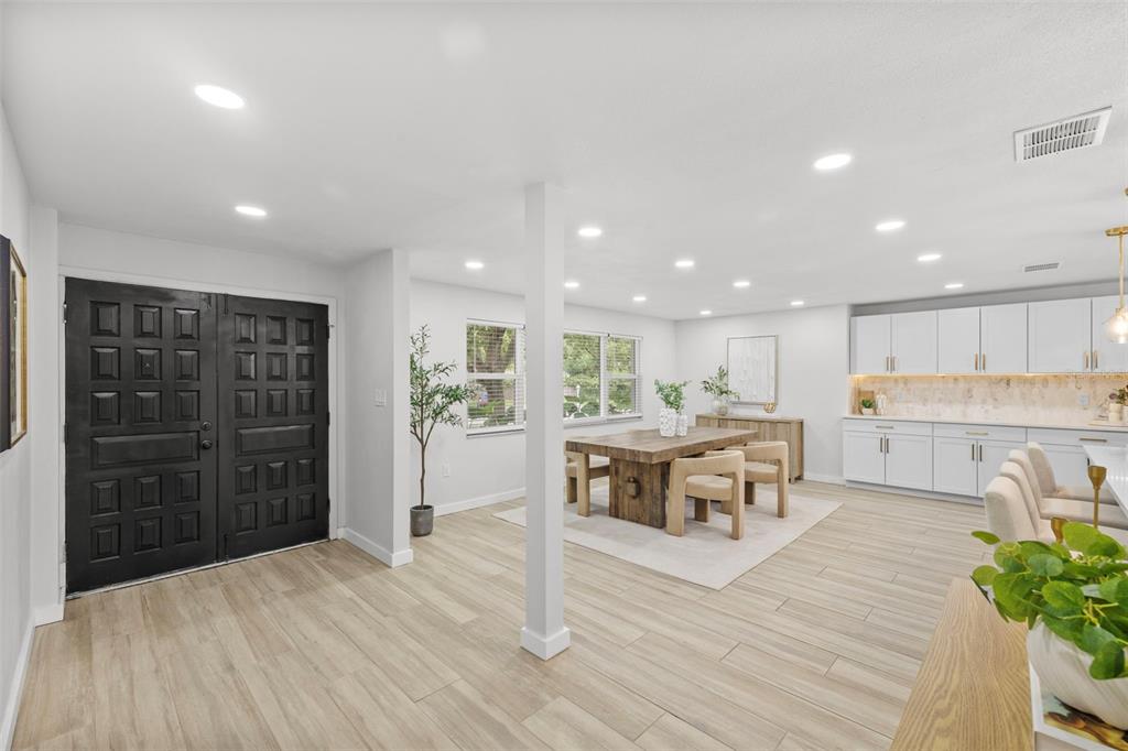 A bright open-concept living space features a black double front door, light wood-look flooring, and white cabinetry — 1905 ORO COURT, CLEARWATER, FL