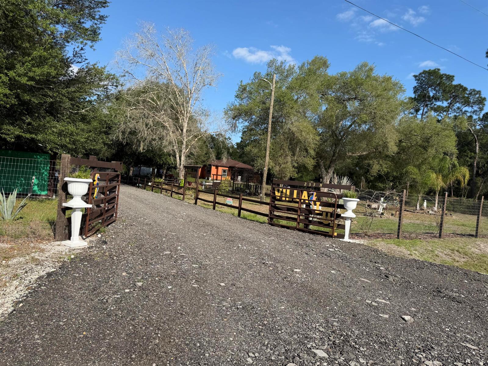 A gravel driveway leads through an open metal gate toward a house and trees — 235 N Sendero Street, Clewiston FL 33440, CLEWISTON, FL