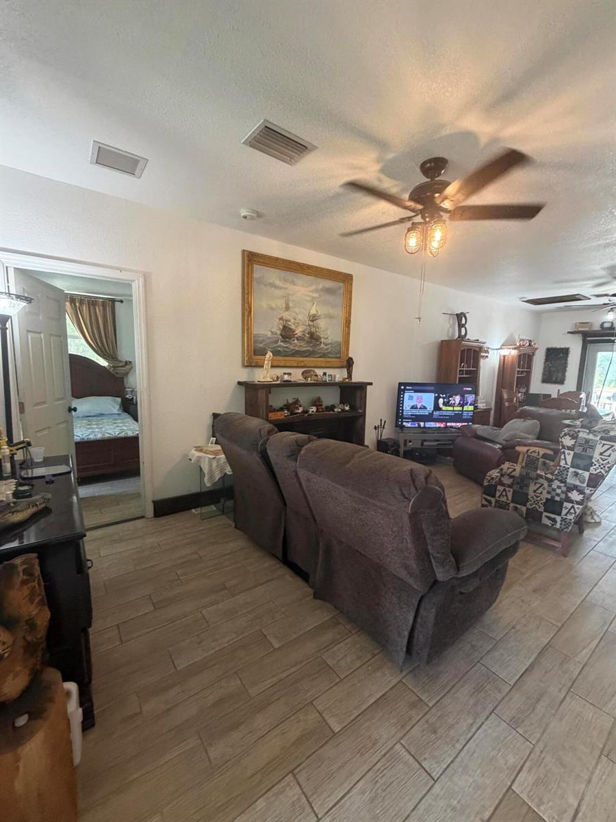 A living room with wood-look tile flooring, a ceiling fan, and a view into a bedroom — 235 N Sendero Street, Clewiston FL 33440, CLEWISTON, FL