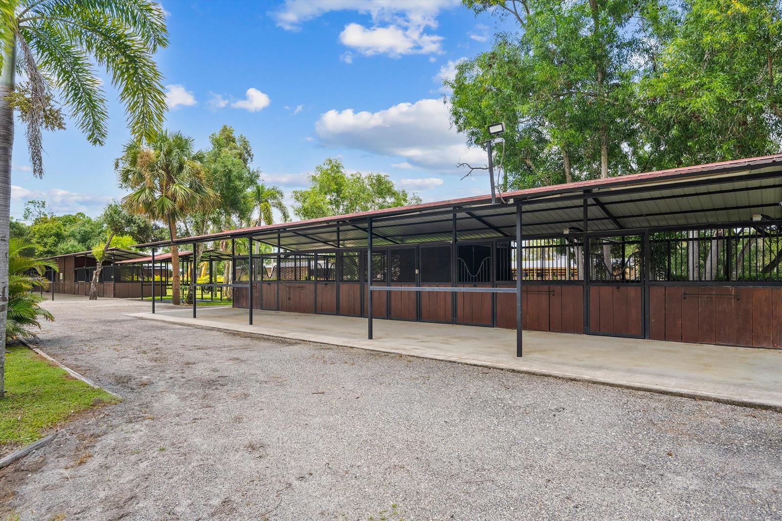 An outdoor horse stable with multiple stalls under a long metal roof — 3570 B Road, FL 33470, FL
