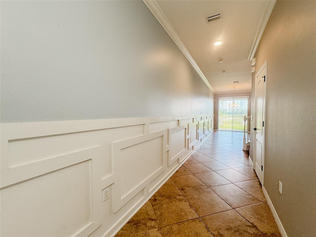 A long hallway features white wainscoting, light blue walls, and brown tile flooring — 27015 JUNIPER BAY DRIVE, WESLEY CHAPEL, FL
