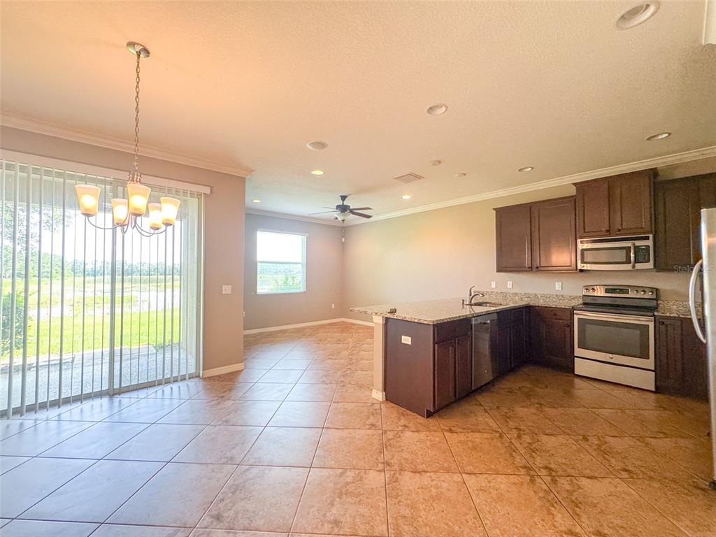 An open-concept kitchen and dining area features dark wood cabinets, granite countertops, and tile flooring — 27015 JUNIPER BAY DRIVE, WESLEY CHAPEL, FL