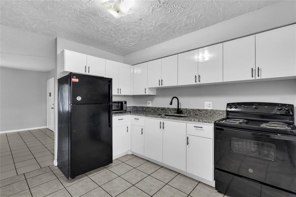 A kitchen features white cabinets, black appliances, granite countertops, and light-colored tile flooring — 1629 W OAK RIDGE ROAD UNIT 1629D, ORLANDO, FL