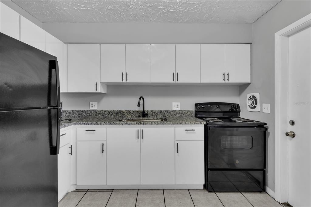 A kitchen features white cabinets, granite countertops, and black appliances against a light gray wall — 1629 W OAK RIDGE ROAD UNIT 1629D, ORLANDO, FL
