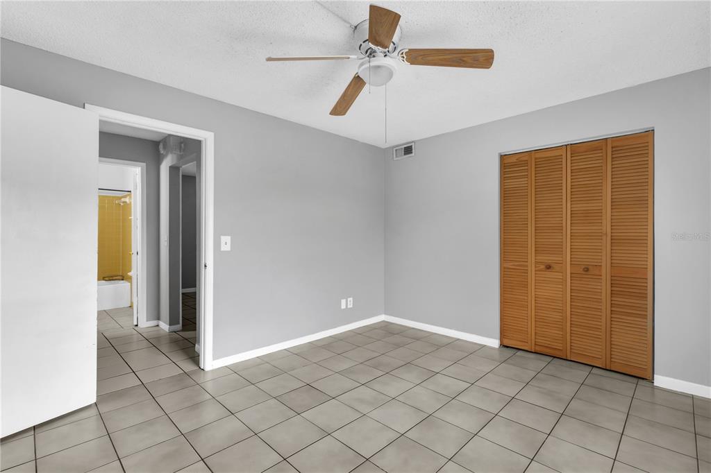 A bedroom with gray walls, light tile flooring, a ceiling fan, and wooden closet doors — 1629 W OAK RIDGE ROAD UNIT 1629D, ORLANDO, FL