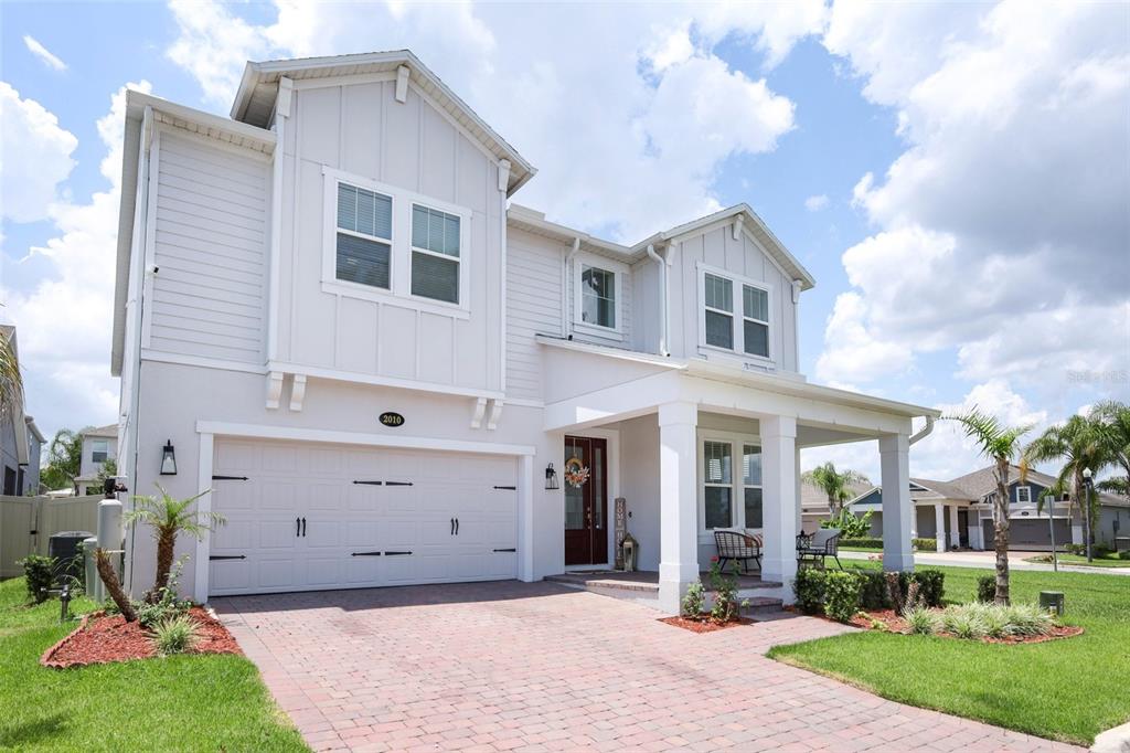A two-story house with light gray siding, a brick paver driveway, and a front porch — 2010 BOSS HEWETT STREET, WINTER GARDEN, FL