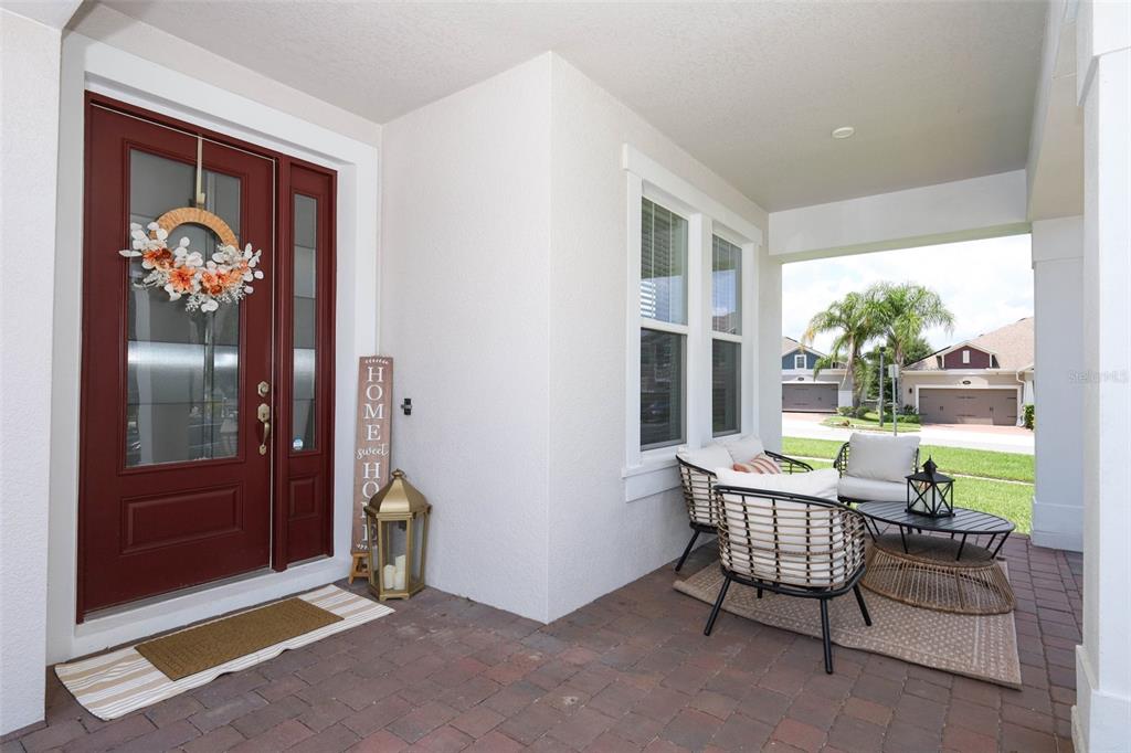 A covered brick porch features a red front door, outdoor seating, and a decorative lantern — 2010 BOSS HEWETT STREET, WINTER GARDEN, FL