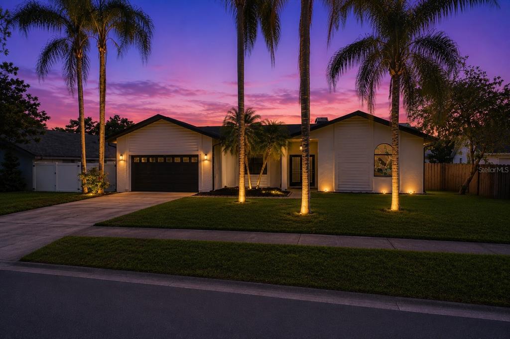 A single-story house with a white exterior, black garage door, and palm trees in front — 2135 VANCE AVENUE, PALM HARBOR, FL