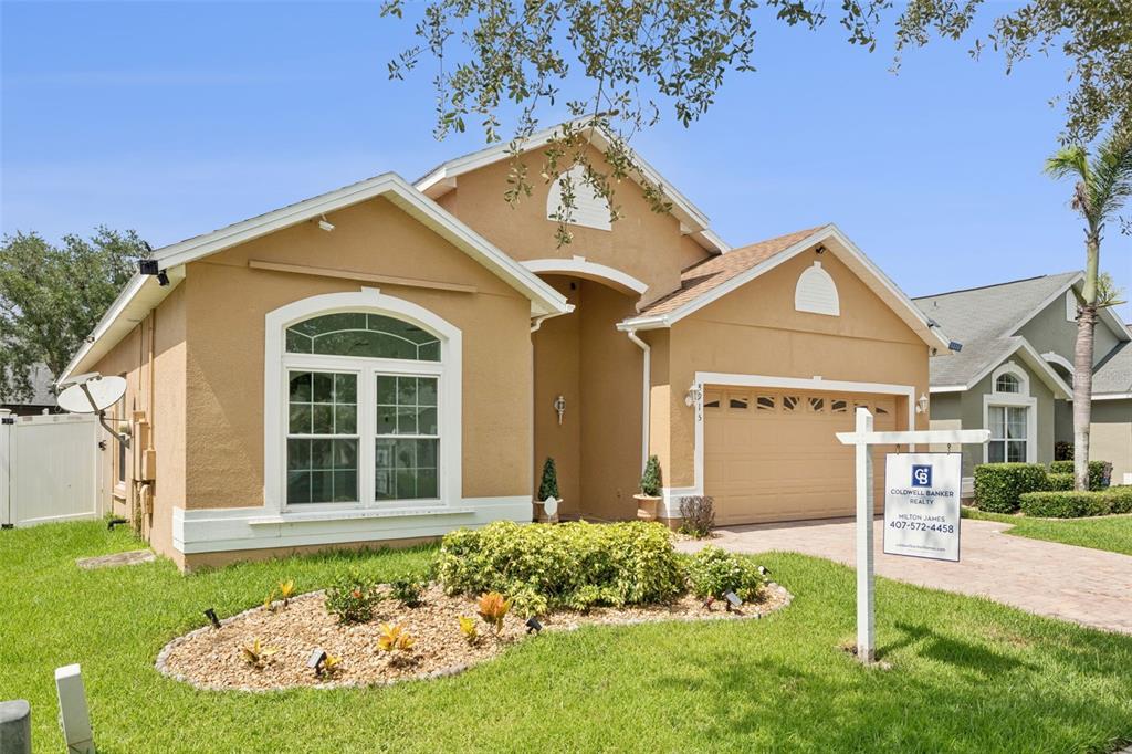 A single-story tan house with a two-car garage and a front yard garden — 8915 VICTORIA ISLE PLACE, ORLANDO, FL
