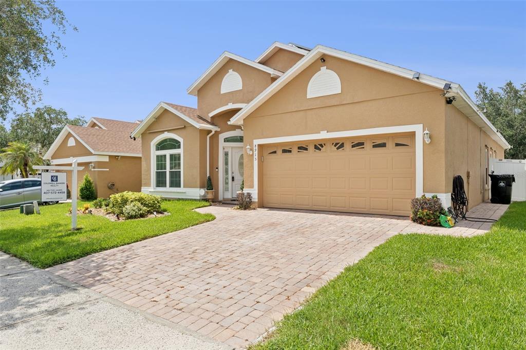 A tan, single-story suburban house features a brick paver driveway and a two-car garage — 8915 VICTORIA ISLE PLACE, ORLANDO, FL