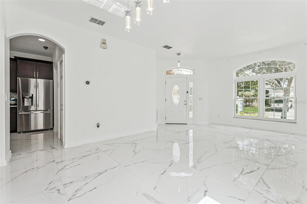 A bright, open-concept room features white marble-look tile flooring, a white front door, and kitchen — 8915 VICTORIA ISLE PLACE, ORLANDO, FL