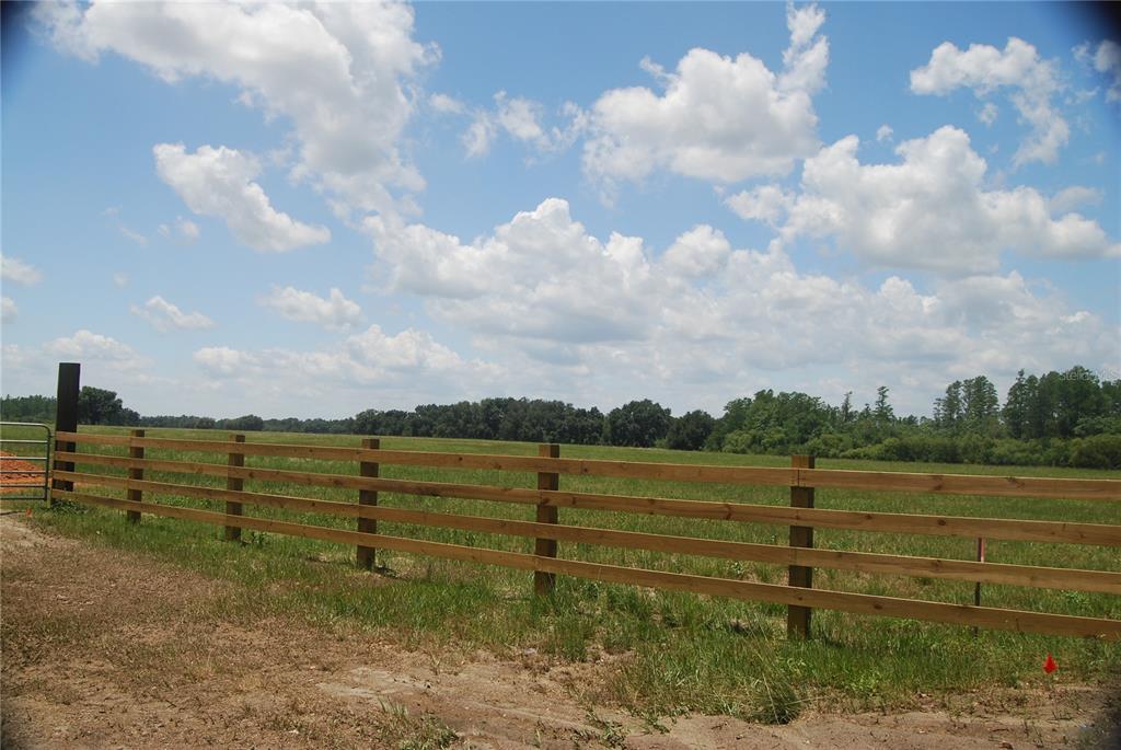 A wooden three-rail fence borders a large, grassy field under a blue sky with clouds — LAKE ERIE ROAD, CLERMONT, FL