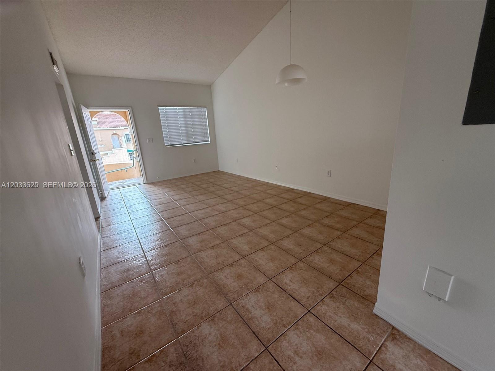 An empty room features tan tile flooring, white walls, a vaulted ceiling, and a doorway — 13120 SW 64th Ter # 1504, Miami FL 33183, MIAMI, FL