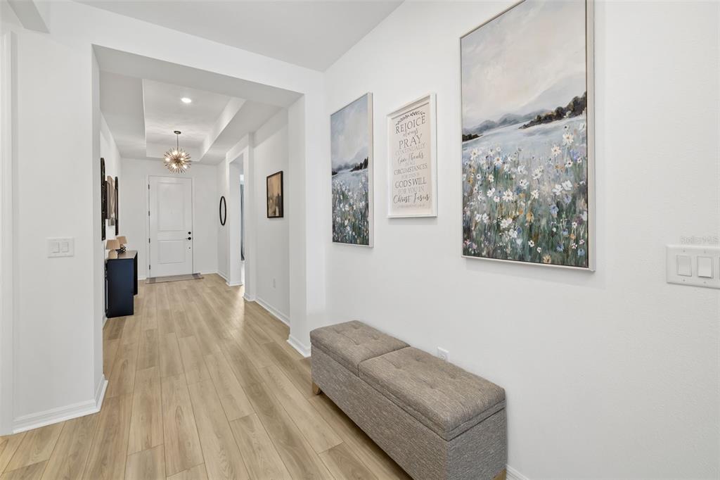 A bright hallway features light wood-look flooring, a gray storage bench, and wall art — 17237 SAVORY MIST CIRCLE, BRADENTON, FL