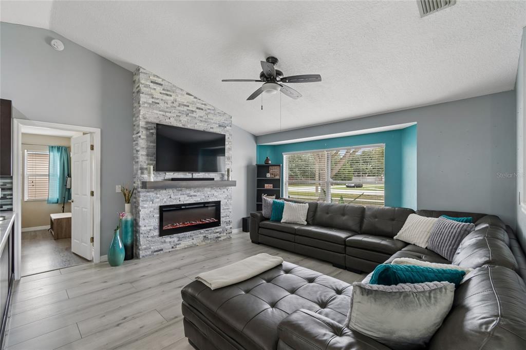 A living room features a stone fireplace, a large sectional sofa, and light wood flooring — 717 LA COSTA STREET, MINNEOLA, FL