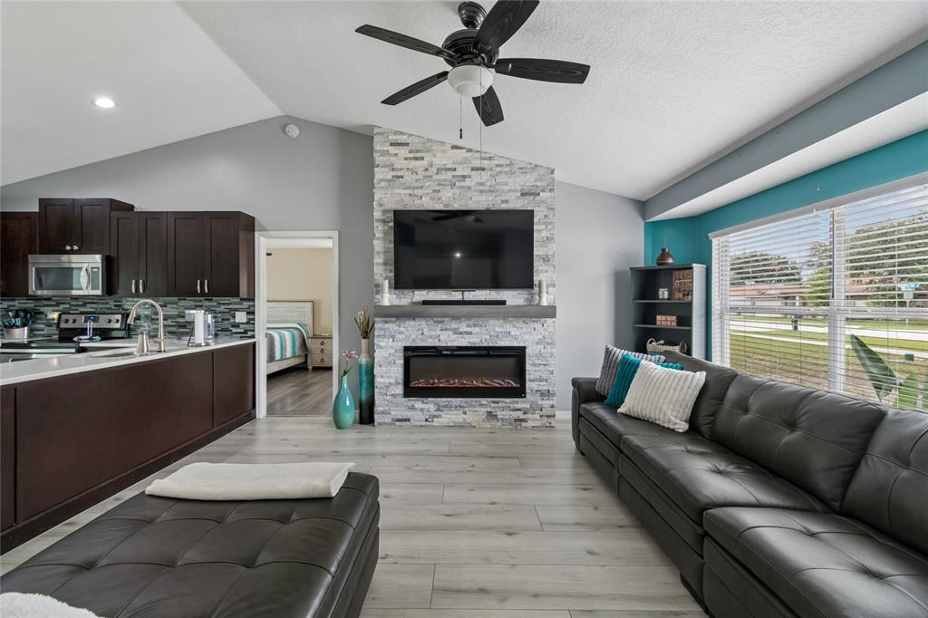 A living room features a stone fireplace, dark cabinetry, and a black leather sofa — 717 LA COSTA STREET, MINNEOLA, FL
