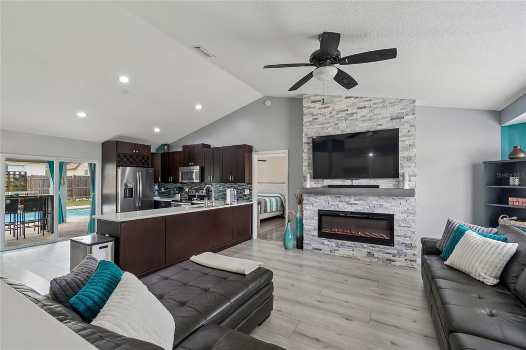A living room with a stone fireplace and television opens to a kitchen with dark cabinets — 717 LA COSTA STREET, MINNEOLA, FL