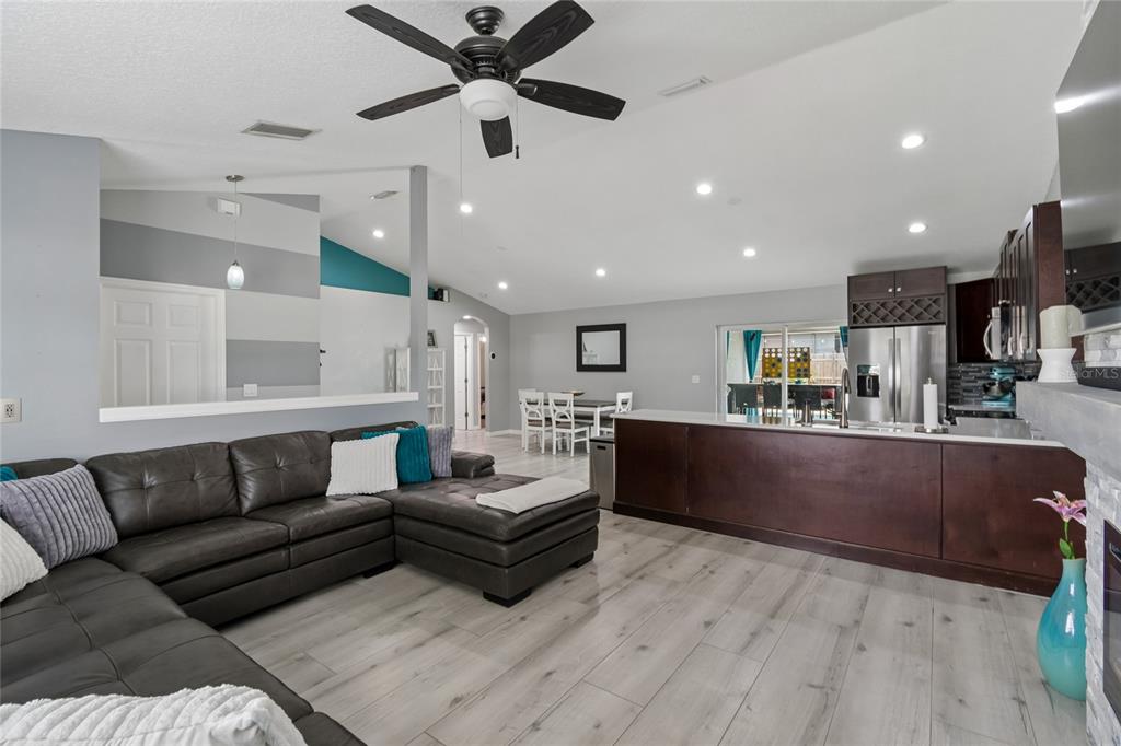 An open-concept living room features a dark leather sectional, wood-look flooring, and a kitchen island — 717 LA COSTA STREET, MINNEOLA, FL