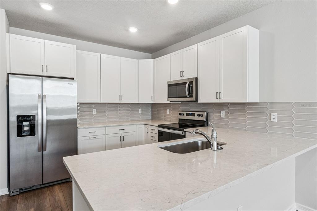 A kitchen features white cabinets, stainless steel appliances, a light-colored countertop, and a tiled backsplash — 14375 SAPELO BEACH DRIVE, ORLANDO, FL