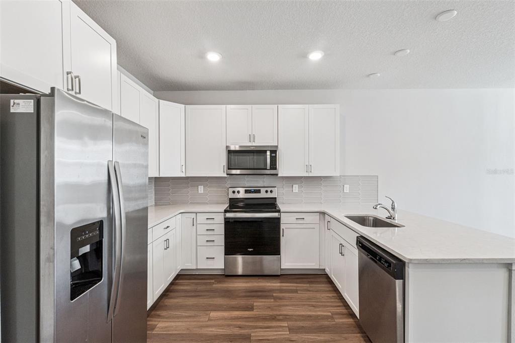 A kitchen with white cabinets, stainless steel appliances, quartz countertops, and wood-look flooring — 14375 SAPELO BEACH DRIVE, ORLANDO, FL