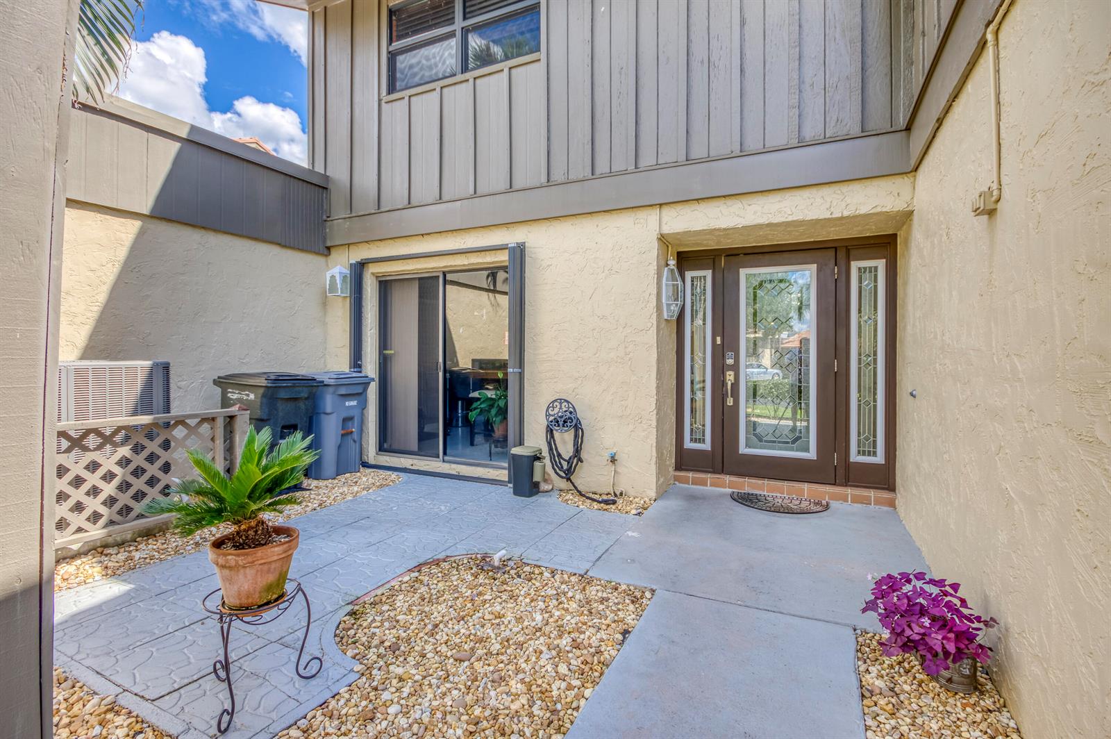 A paved entryway features a front door, a sliding glass door, and gravel landscaping — 11135 Oakdale Road, Boynton Beach FL 33437, BOYNTON BEACH, FL