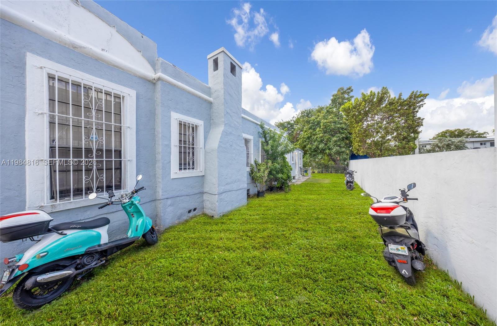 A light blue house exterior features a chimney and two parked scooters on the grass — 844 NW 29th St, Miami FL 33127, MIAMI, FL