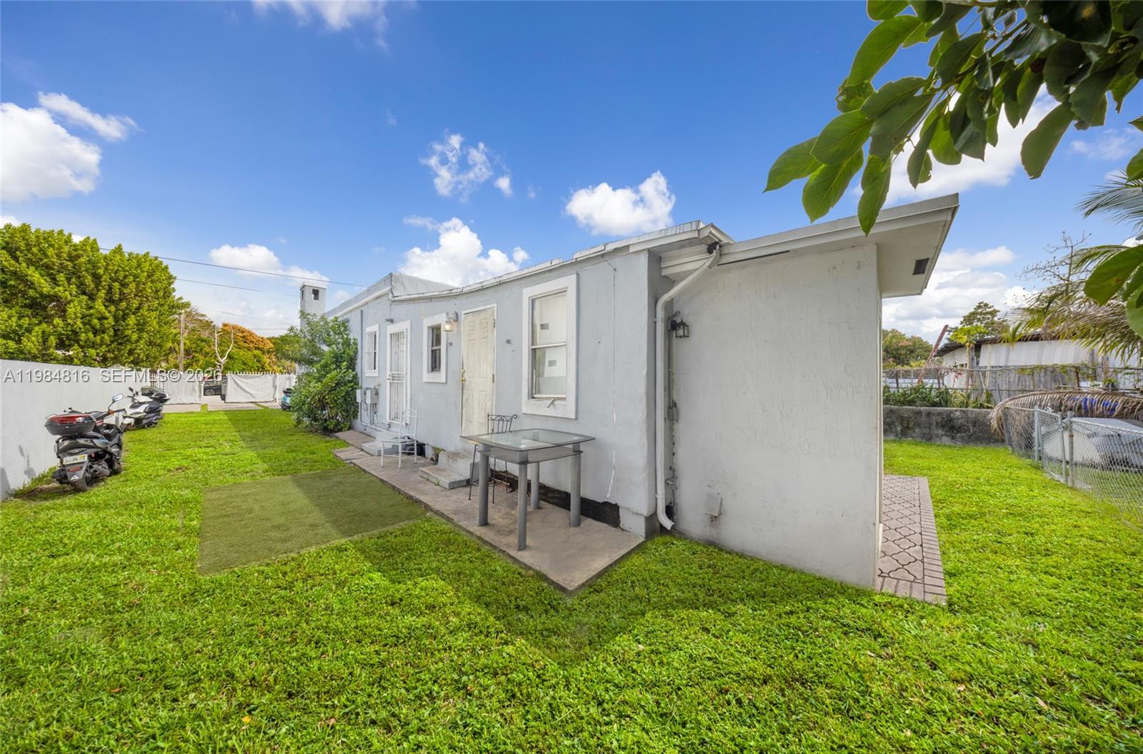 The exterior of a light-colored, single-story house features a small patio and a grassy yard — 844 NW 29th St, Miami FL 33127, MIAMI, FL