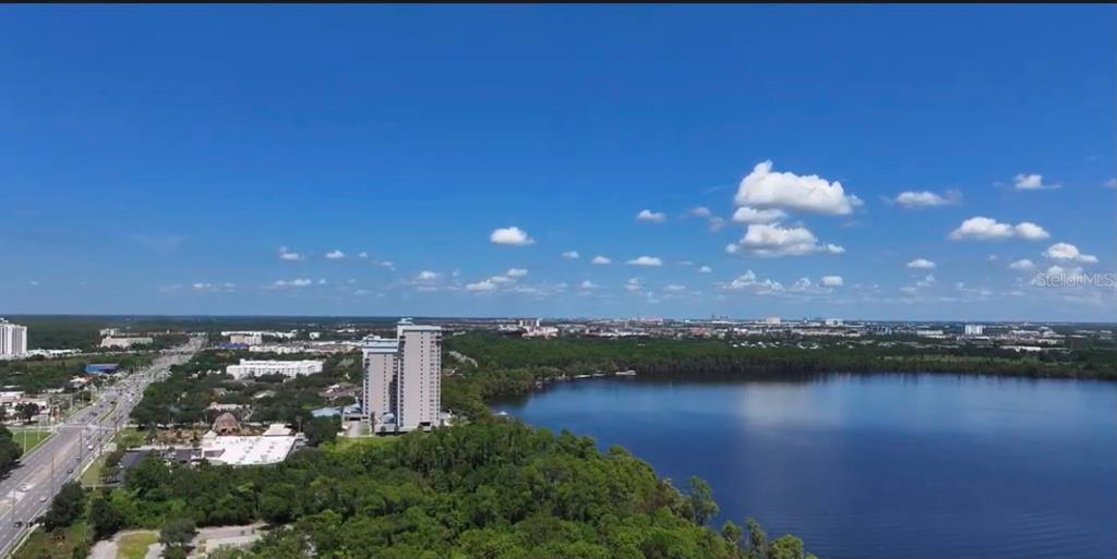 An aerial view shows a lake in the foreground with high-rise buildings and surrounding landscape — 13709 S APOPKA VINELAND ROADS, ORLANDO, FL
