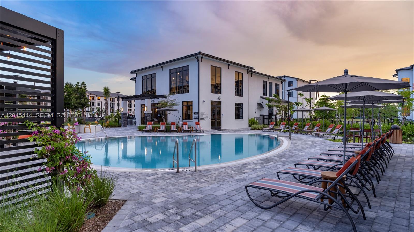 A swimming pool with lounge chairs and umbrellas sits in front of a modern building — 9030 SW 158th Ave # 211, Miami FL 33196, MIAMI, FL