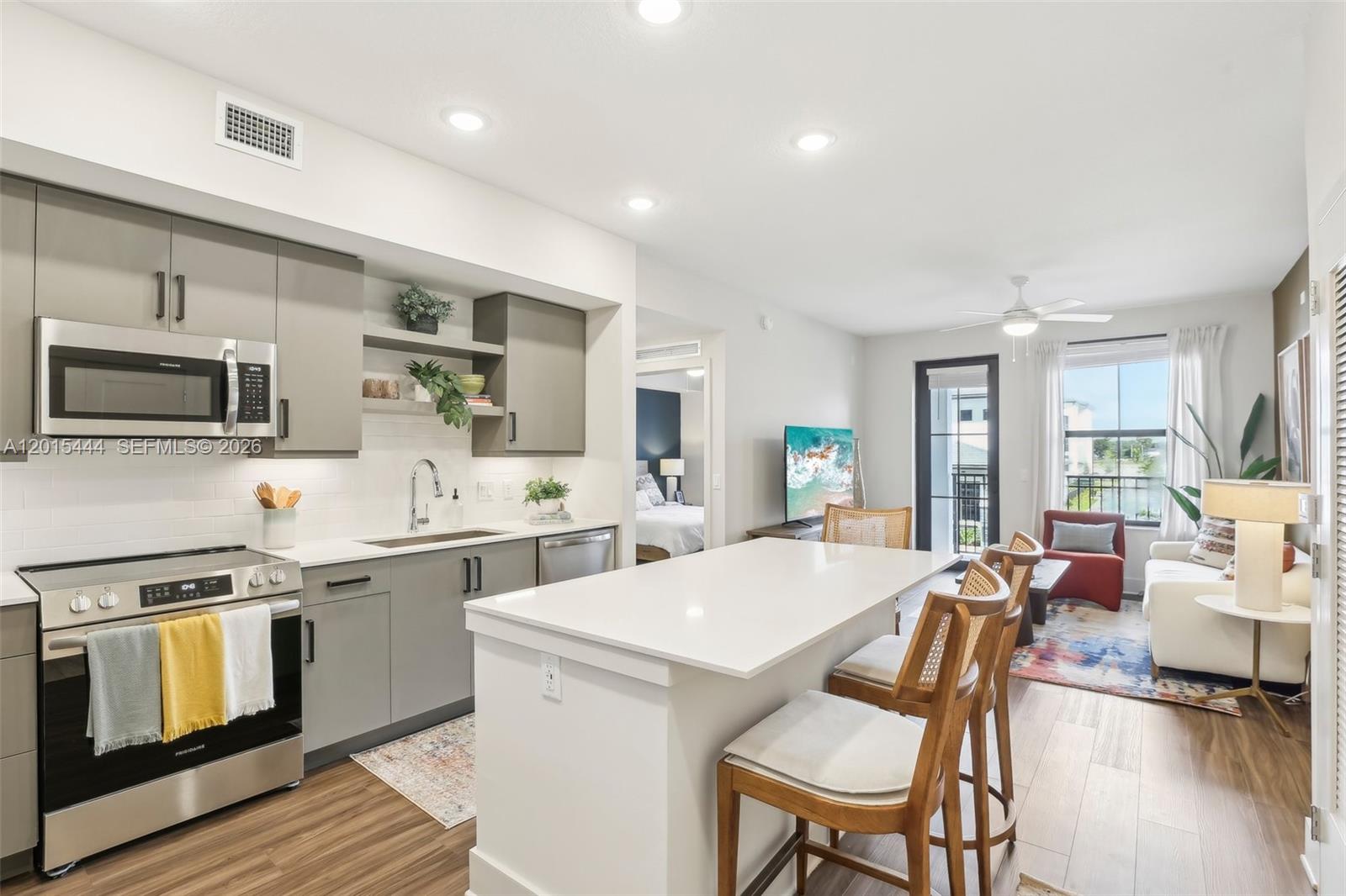 A modern kitchen with gray cabinets and a white island opens into a living area — 9030 SW 158th Ave # 211, Miami FL 33196, MIAMI, FL