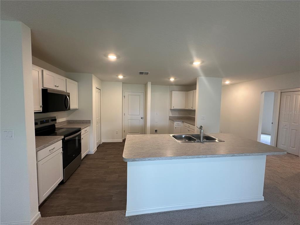 A kitchen features white cabinets, stainless steel appliances, a center island, and wood-look flooring — 18 PICKWOOD PLACE, PALM COAST, FL