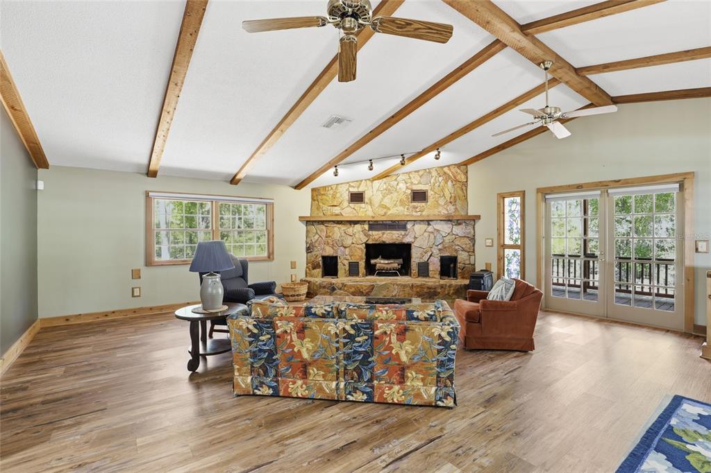 A living room features a stone fireplace, vaulted wood-beamed ceilings, and wood-look flooring — 818 NE 783 STREET, OLD TOWN, FL