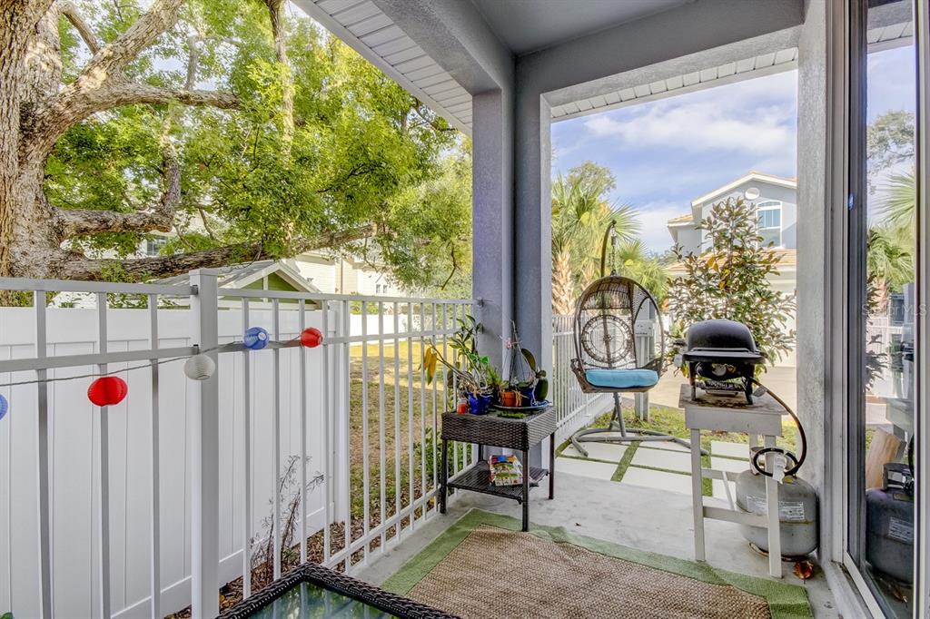 A covered patio features a white metal railing, a hanging chair, and a small grill — 426 BIRDSONG LANE, DUNEDIN, FL