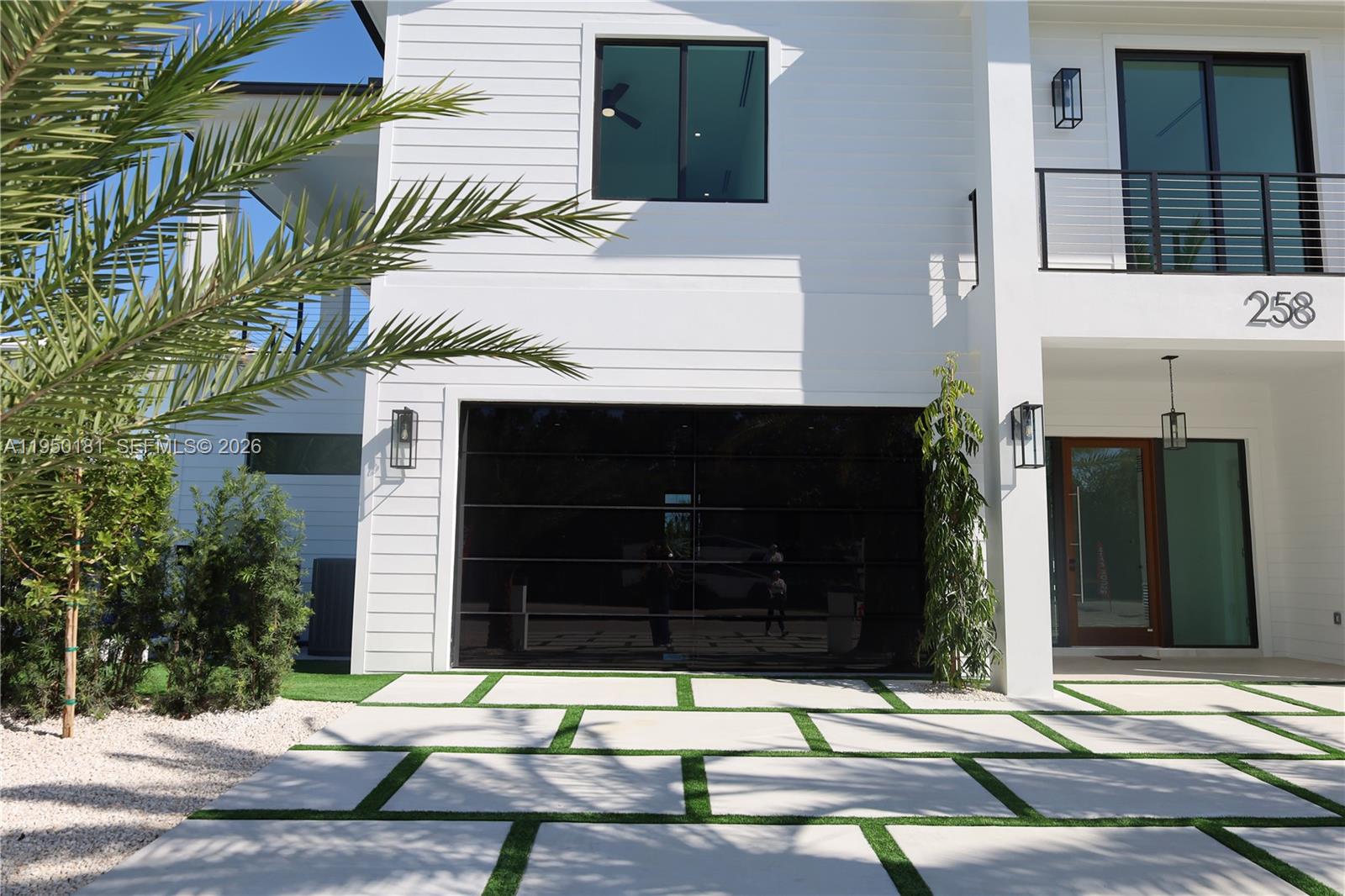 The exterior of a modern white house features a glass garage door and a paved driveway — 258 Caribbean Dr, Key Largo FL 33037, KEY LARGO, FL